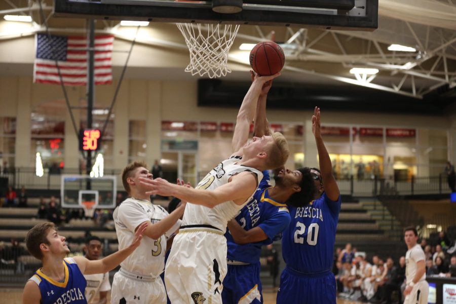 Chandler Diekvoss attempts a layup while being defended by two players from Brescia University. Photo by Carly Fristoe