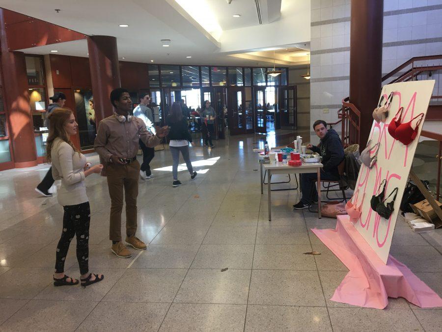 Delta Zeta member Jessie Basler assists junior Ashraf Ahmed as he tries to throws ping pong balls into bras Oct. 25 in Spellmann Center. Delta Zata and Delta Tau Delta joined up to raise funds for breast cancer research with the bra pong game.  Photo by Ciara Griffin
