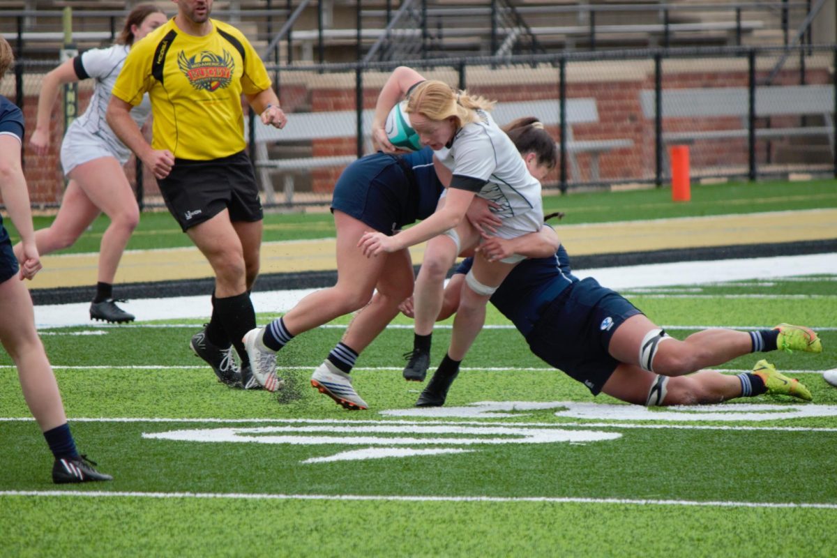 A Lindenwood rugby player is tackled by two BYU defenders while carrying the ball. 