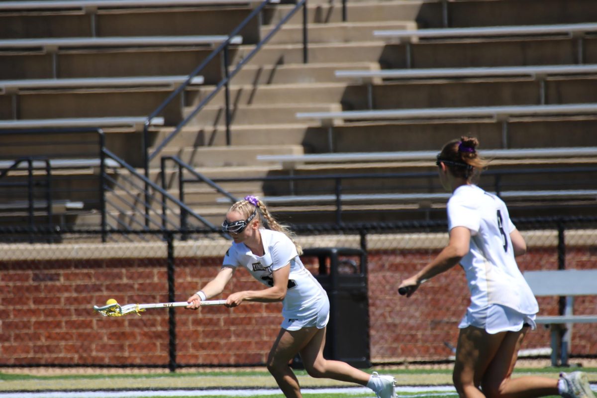 Two Lindenwood Lions women’s lacrosse team members pass the ball towards each other.